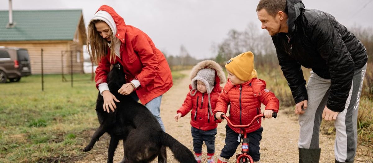 A family bonding outdoors with children playing and a pet dog in the countryside.