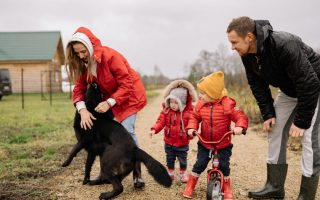 A family bonding outdoors with children playing and a pet dog in the countryside.